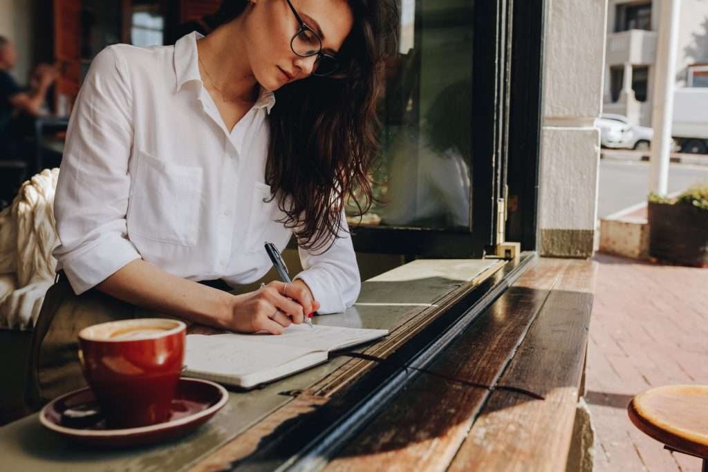 a woman taking notes for her book while sitting in the cafe
