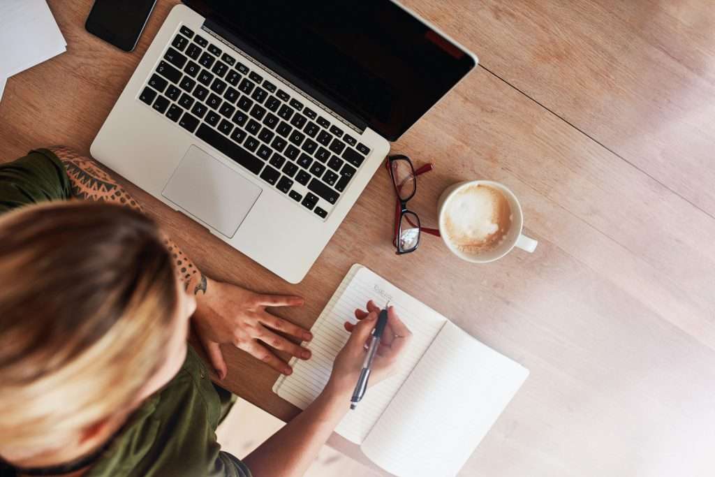 a woman writing on her laptop and taking notes for her book